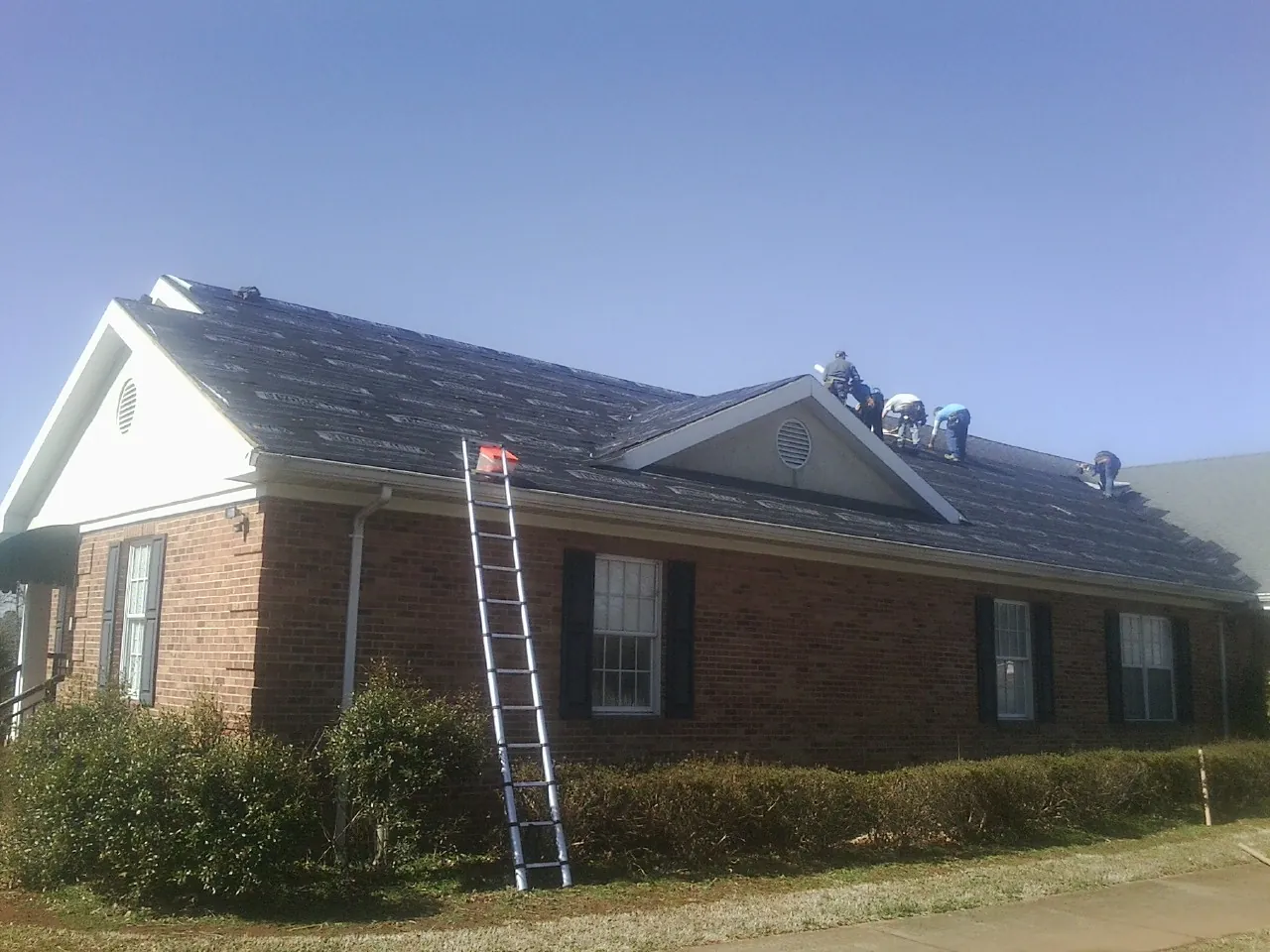 Crew tearing shingles off a brick ranch roof with a ladder set — Emergency Roof Repair work by our crew in Bucoda