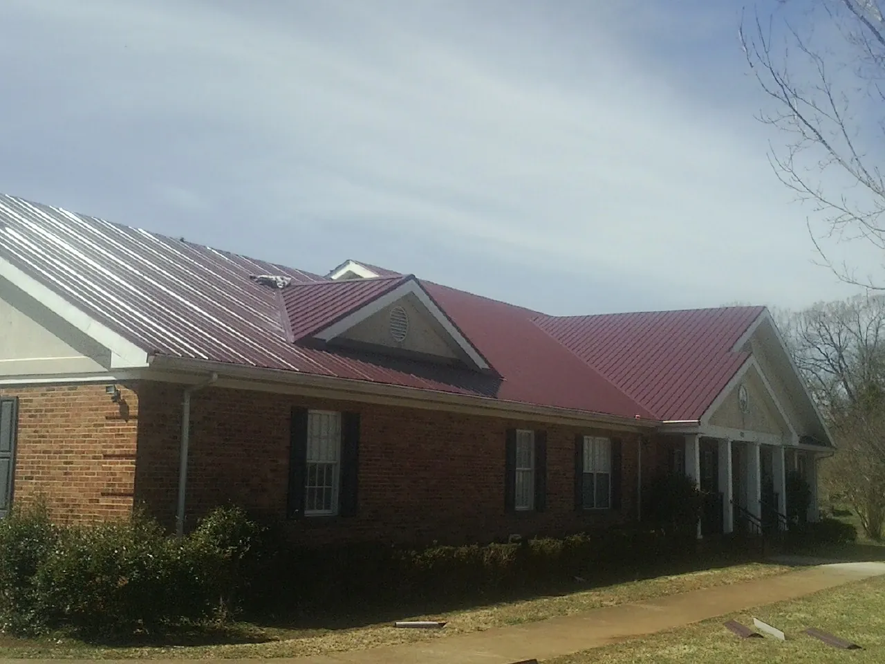 Red metal roof with gabled entries on a long brick building, from a Hail Damage Roof Repair job in Bucoda