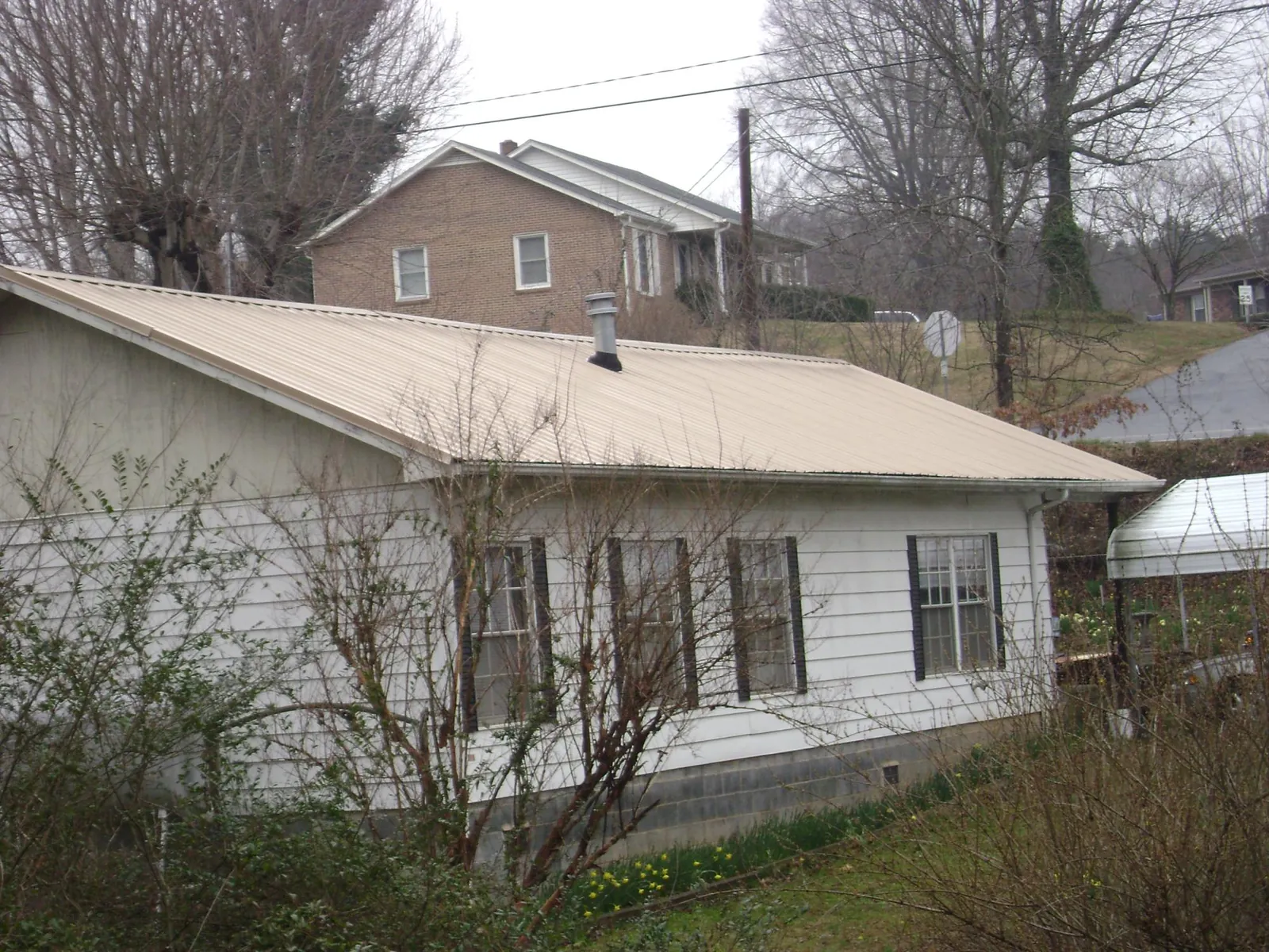 Tan metal roof on a white sided house set into a hillside — Commercial Roofing by Roofing Brothers in Bucoda